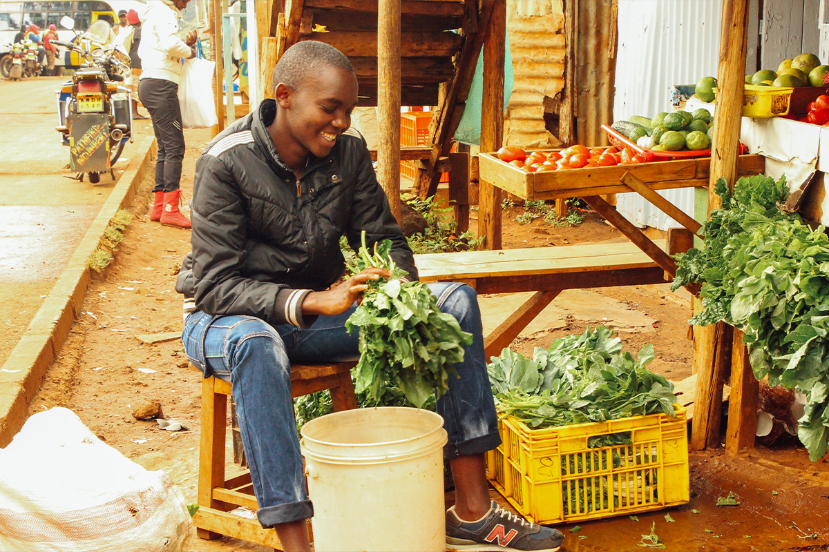 Sponsored  youth Wycliff, 18, who’s also an Unbound scholarship student, cleans produce at the fruit and vegetable stand his mother operates in Nairobi, Kenya.
